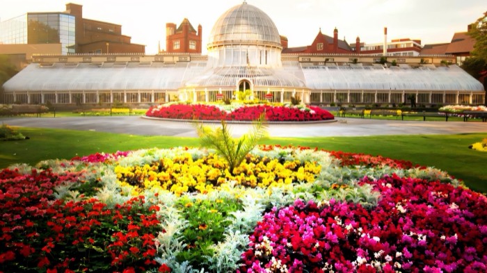 The Victorian Palm House glasshouse behind bright flowerbeds in Botanic Gardens