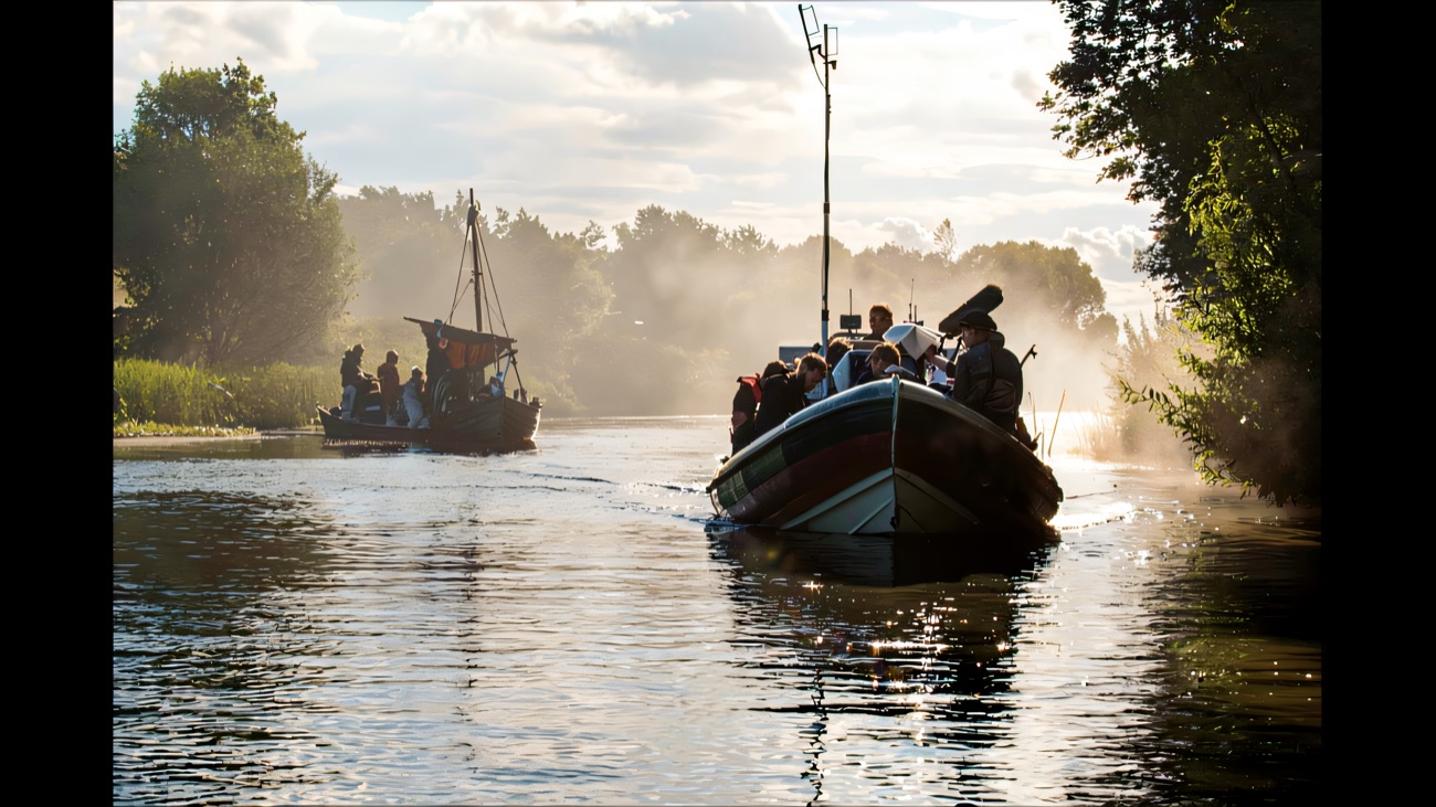Two boats glide up a misty, tree-lined stretch of water in the early light