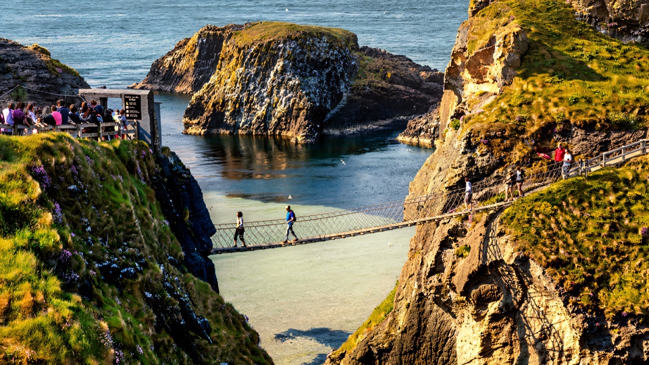 Walkers crossing the Carrick-a-Rede rope bridge high above clear green water