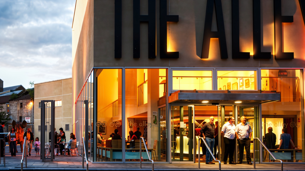 The Alley Arts Centre lit up at dusk, its glass foyer glowing over Strabane