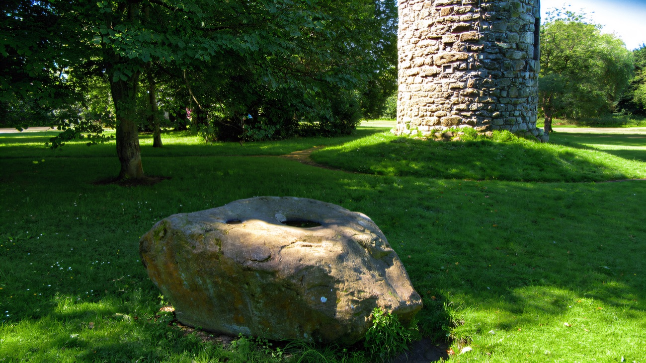 The old bullaun stone on the grass nearby, its hollow said to hold curing water