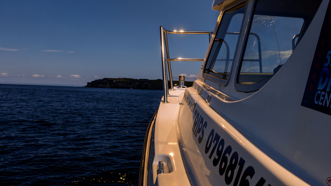 The dive and sea safari boat running along the coast on a bright blue day, headland in the distance
