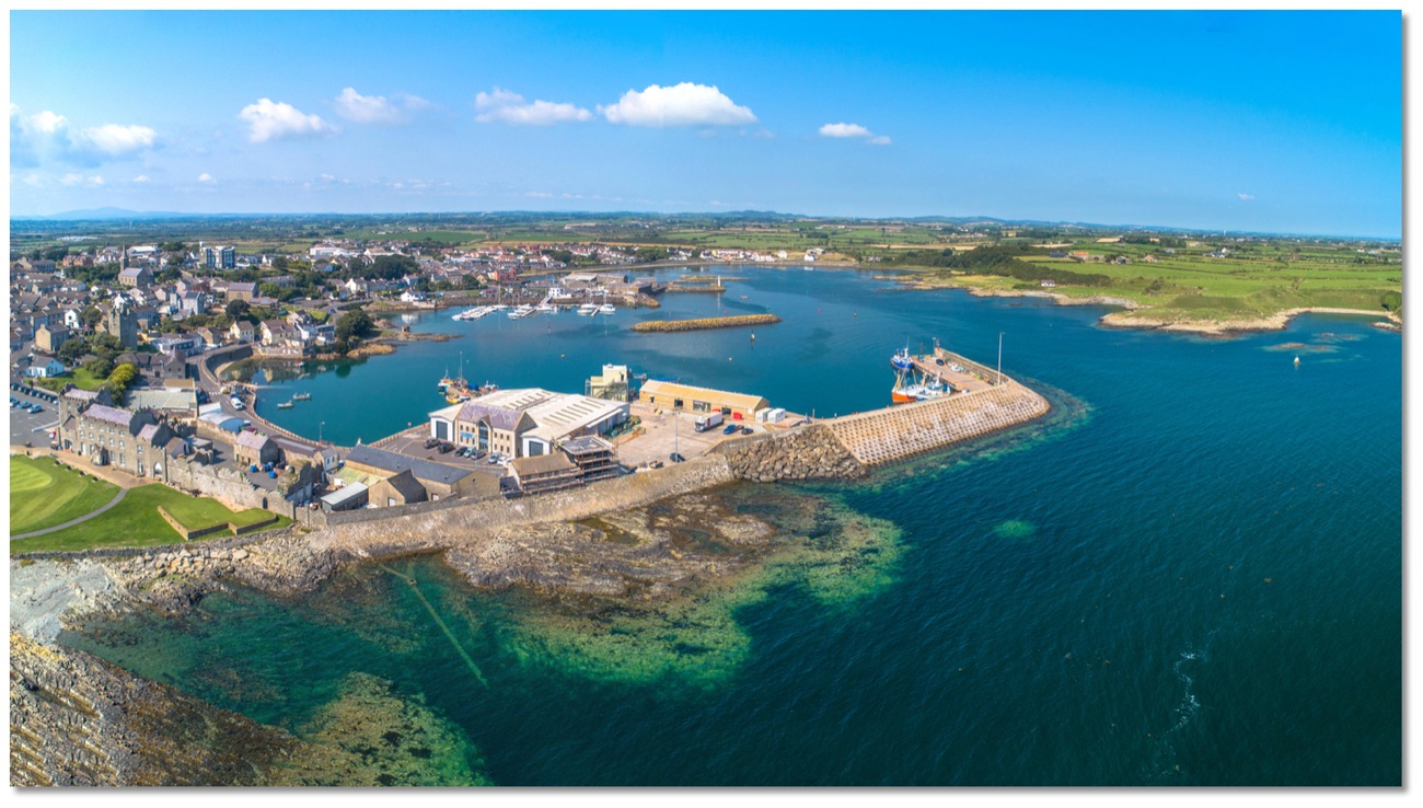 Aerial view over Ardglass harbour and marina with fishing boats, the stone pier and the village behind