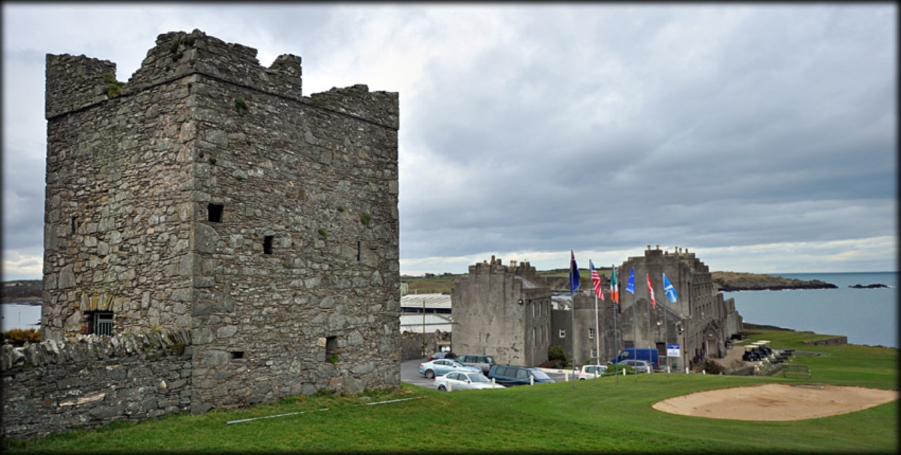 A medieval stone tower house standing beside the Ardglass Golf Club clubhouse under a moody sky