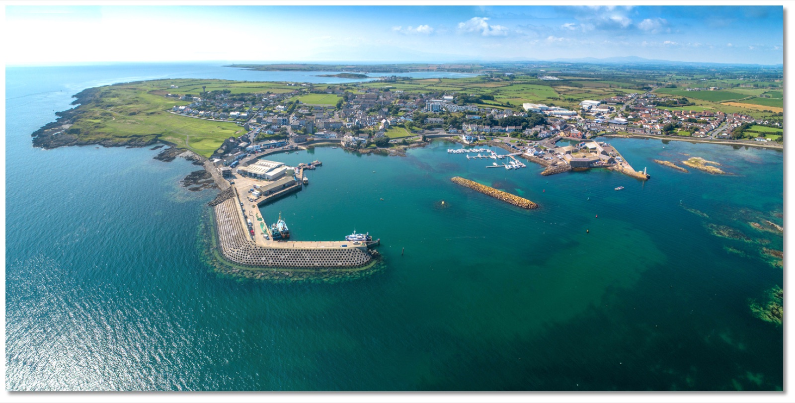 Aerial view of Ardglass harbour and marina wrapping around the fishing village on the Lecale coast under a bright blue sky
