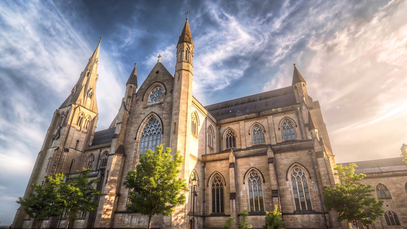 A moody view from the plaza, the buttressed walls and spire catching a wide evening sky.
