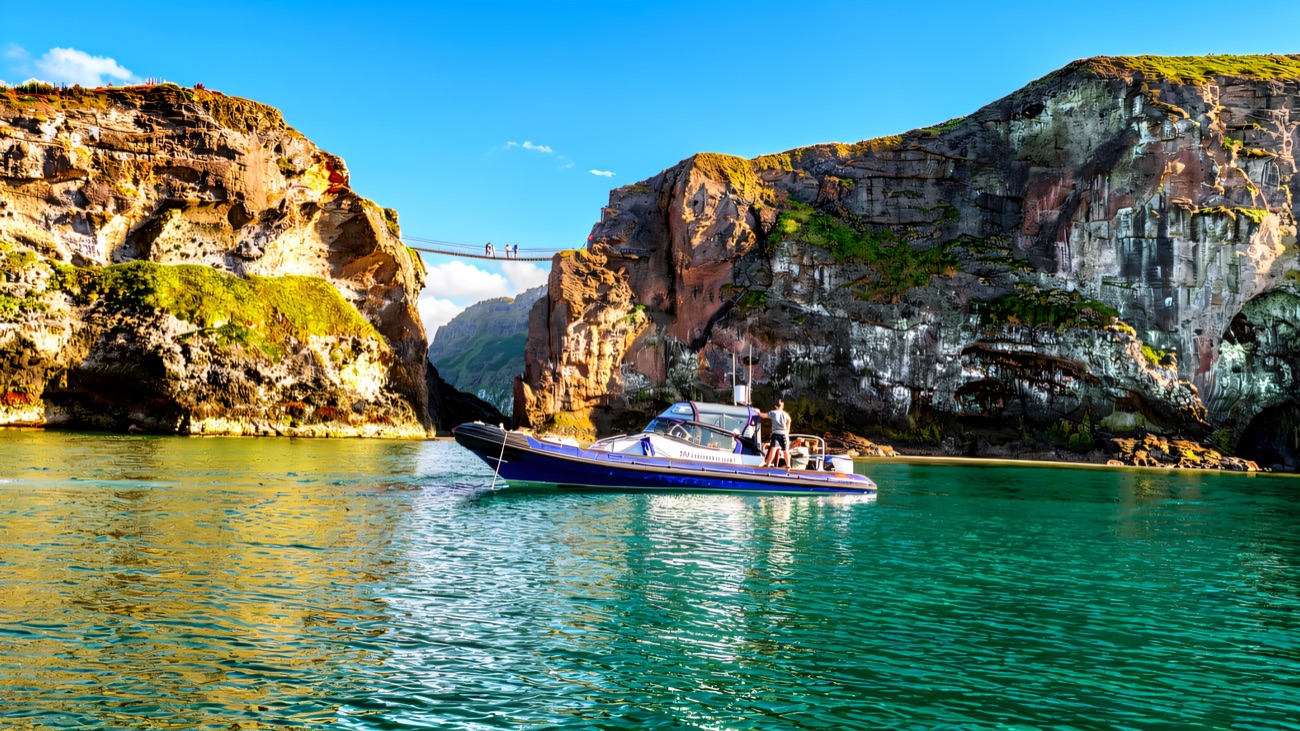 The boat sits on turquoise water right beneath the Carrick-a-Rede rope bridge