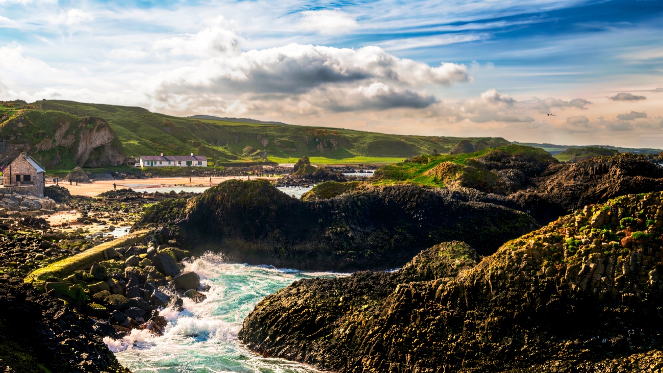 Waves surging between dark basalt rocks below the green cliffs of the Causeway Coast at Ballintoy