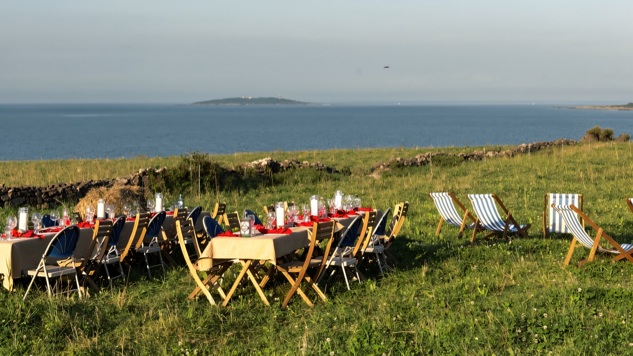 A long outdoor dining table dressed with lanterns and red runners, striped deckchairs beside it, set in a field looking straight out over Strangford Lough