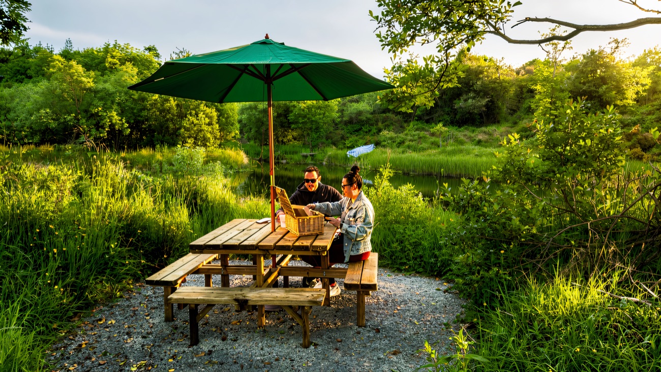 A wooden picnic table under a green parasol beside the pond on the Ballyburren trail