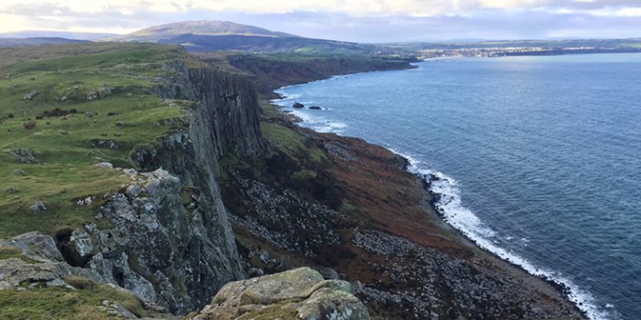 The dark cliff of Fair Head rising above the sea with Ballycastle town across the bay