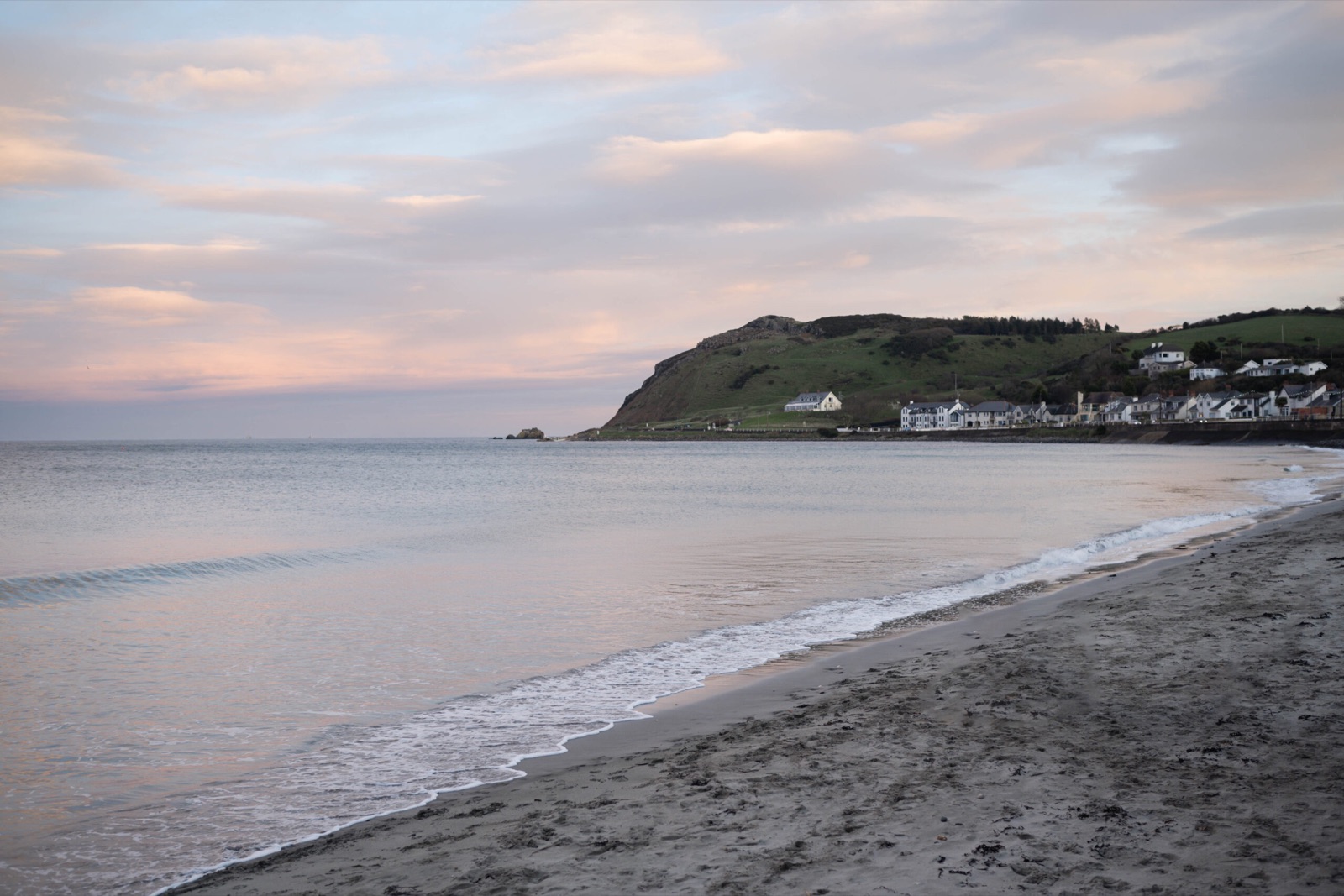 The sandy beach at Ballygally in soft evening light, the headland and seafront village behind the bay