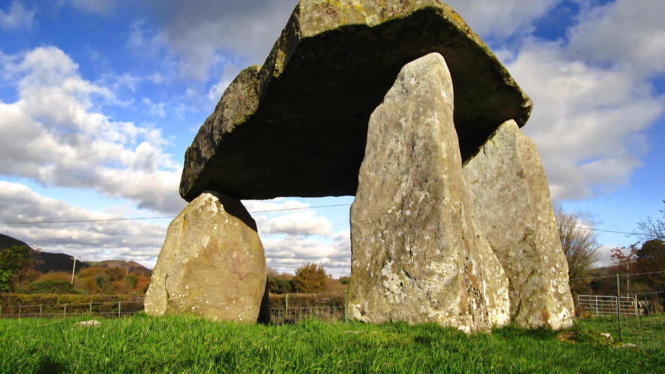 Looking up at the tripod dolmen against a big cloud-filled sky