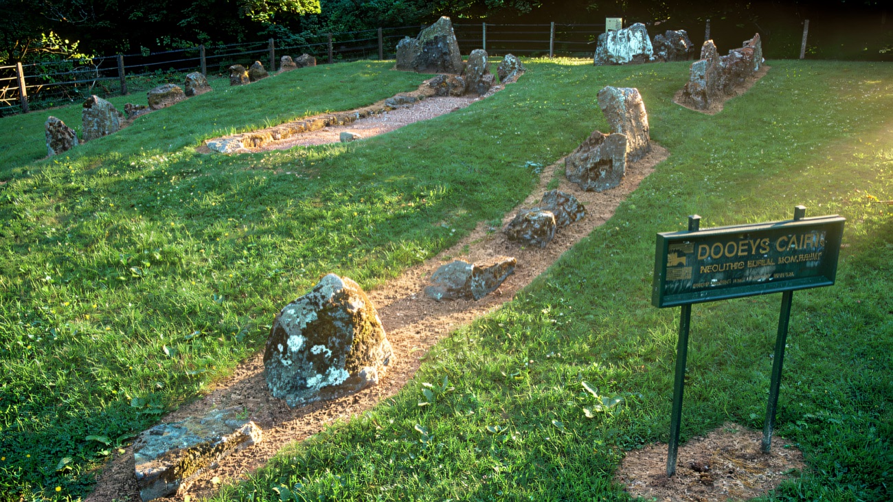 The line of standing stones and low kerbstones on mown grass, with the Dooey's Cairn monument sign alongside