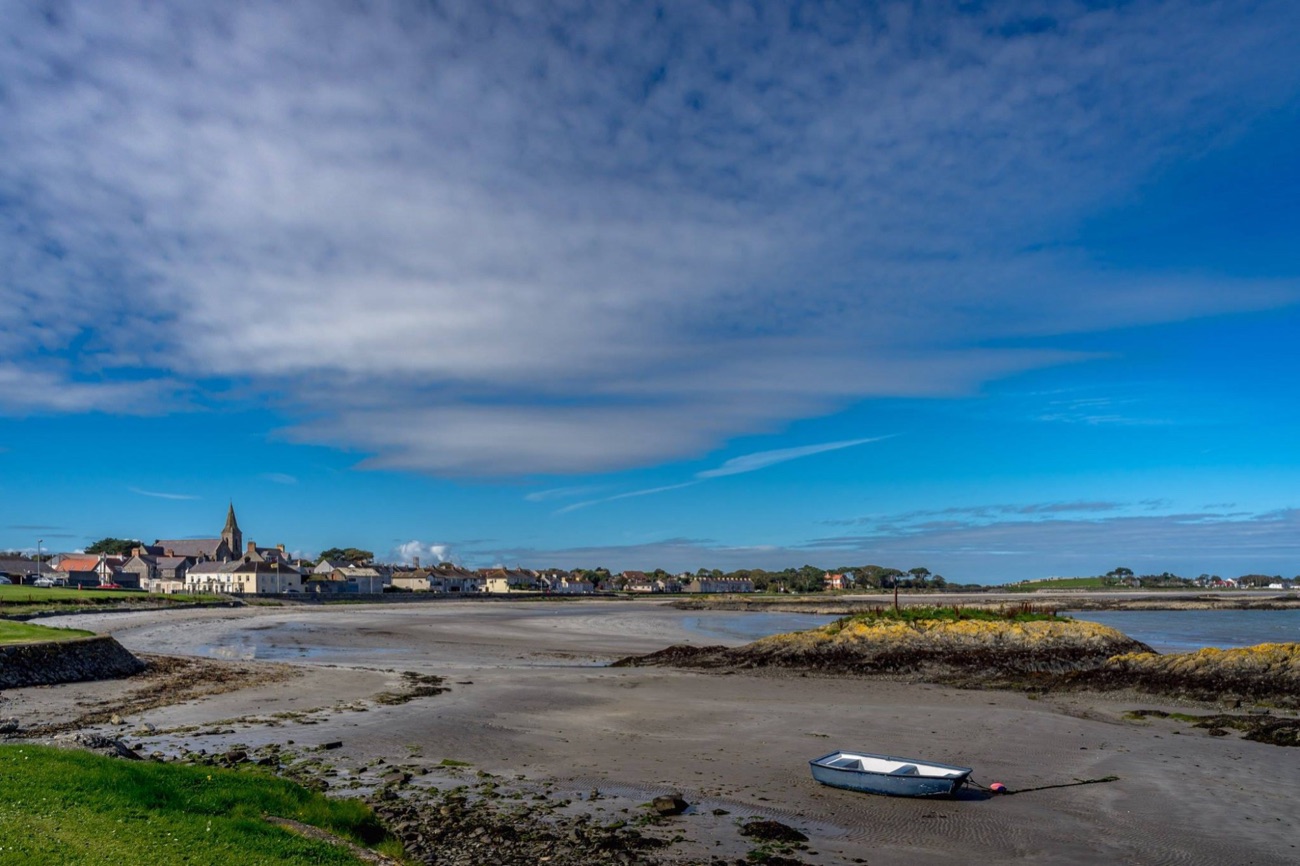 The wide sandy shore at Ballywalter with a single boat, the village and church spire in the distance under a bright blue sky