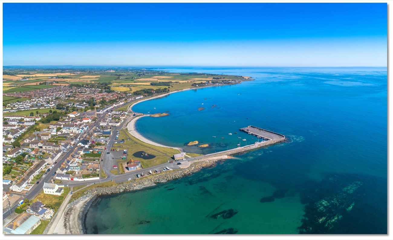 Aerial view of Ballywalter village, its harbour pier and the curving sandy bay meeting the turquoise Irish Sea