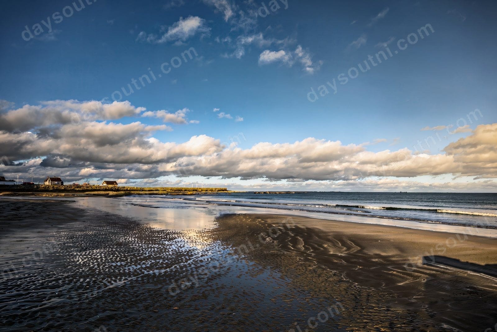 The long sandy beach at Ballywalter at low tide with the harbour wall and village along the shore under a big cloud-streaked sky