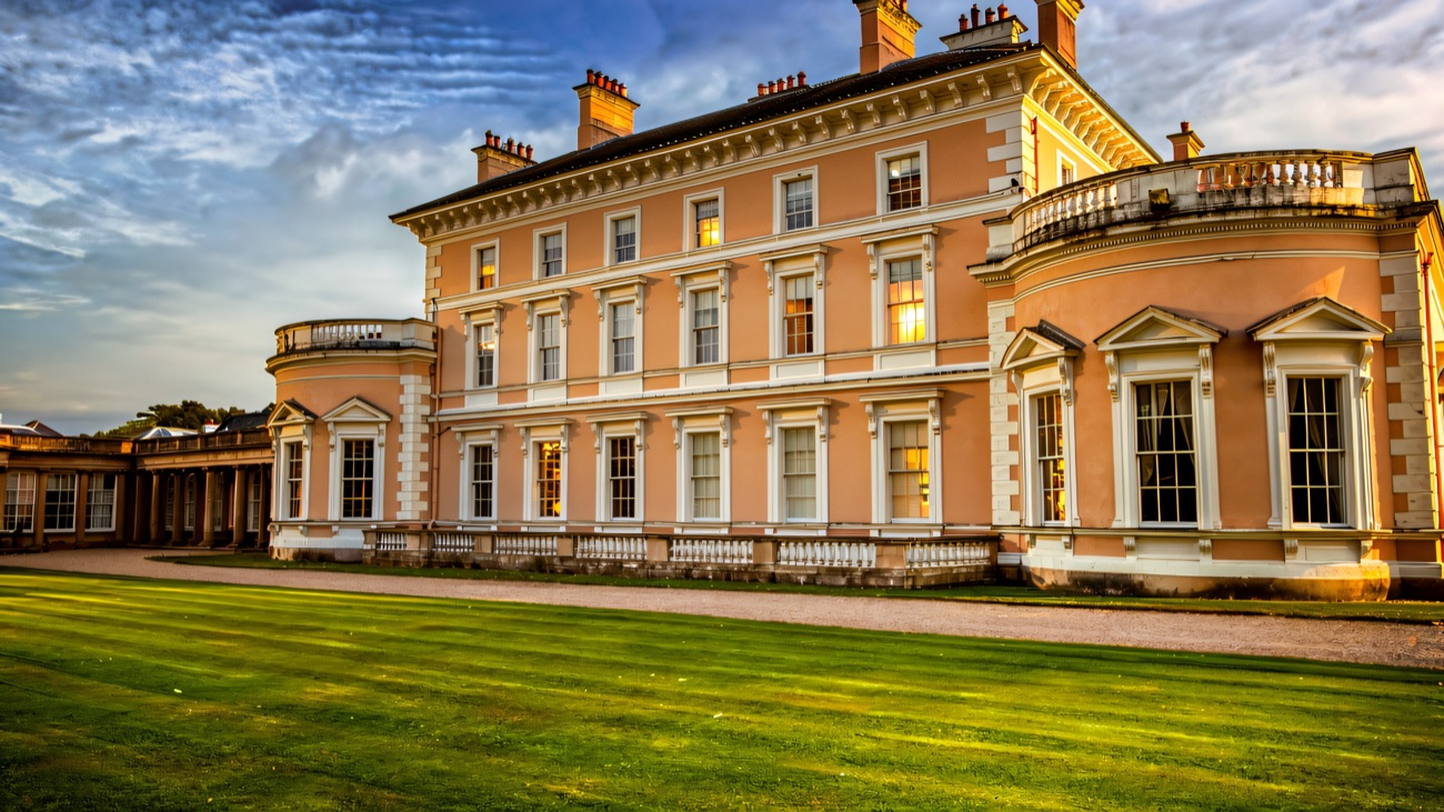The side elevation of Ballywalter Park mansion across a wide sweep of parkland lawn under blue sky