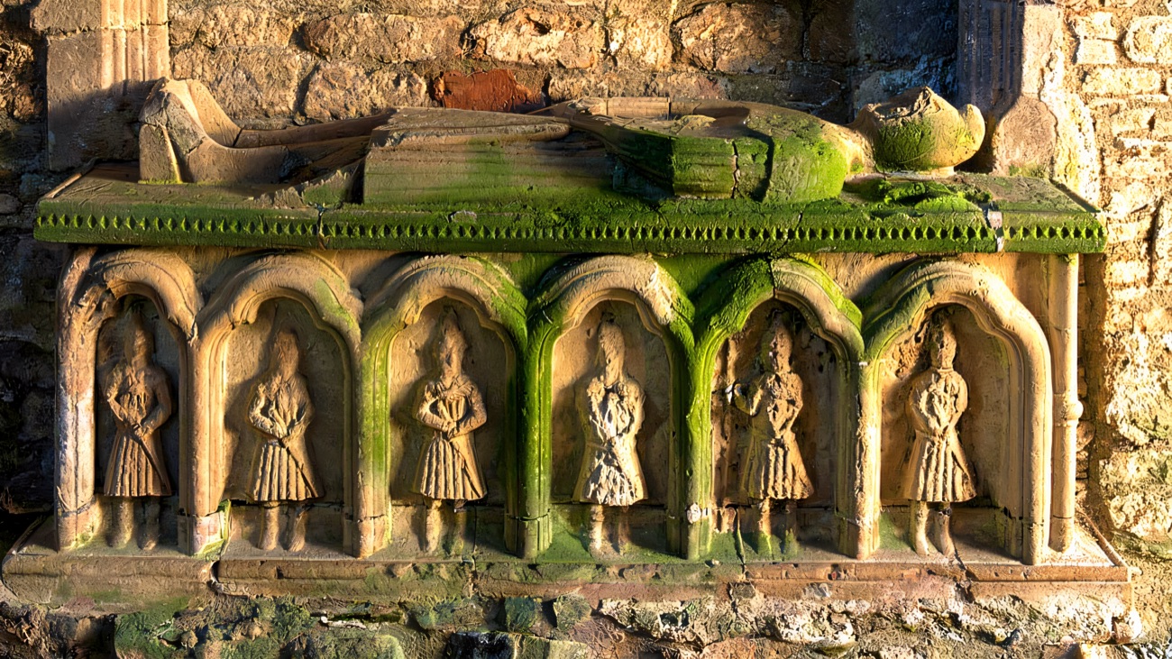 The carved mortuary house nearby, its little arcaded figures softened by green moss