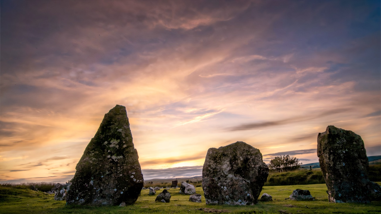 The taller standing stones silhouetted against a warm sunset sky.