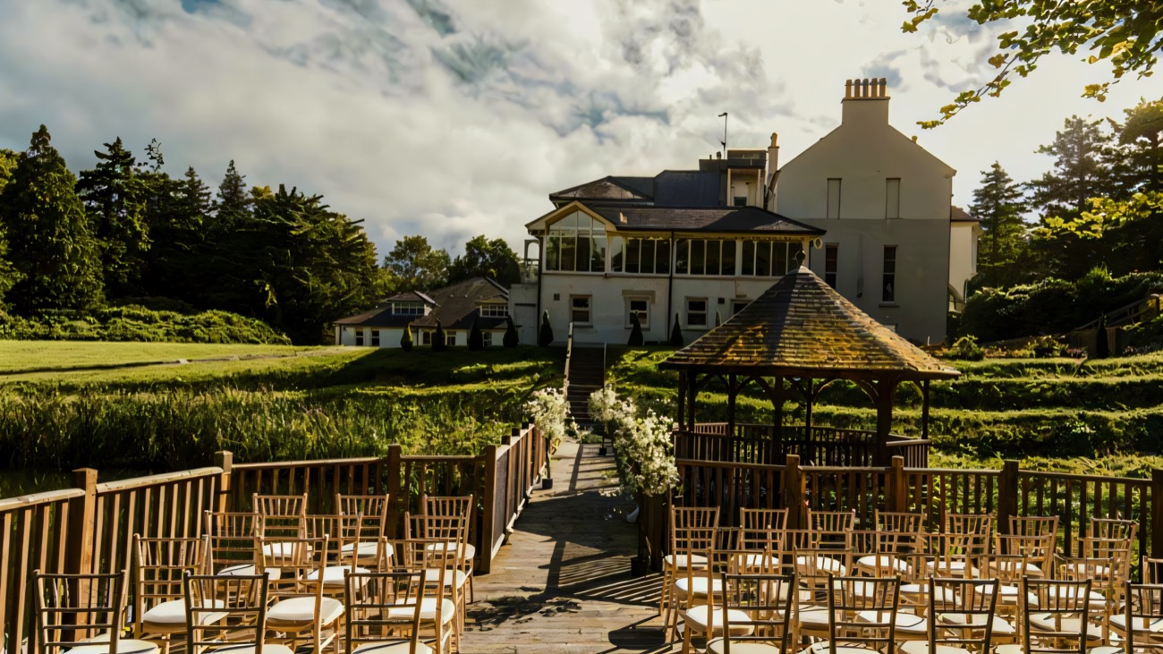 A wooden boardwalk and gazebo set out over the water in the grounds of Beech Hill, with the house rising behind