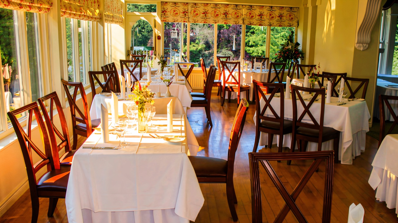 A bright conservatory dining room at Beech Hill, tables laid in white linen with windows looking out over the gardens