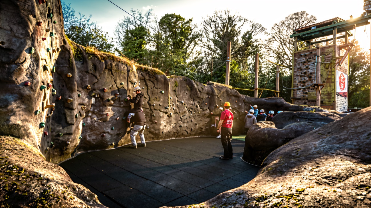The outdoor climbing wall built into a rock bowl, with matting on the floor and a high ropes tower behind.