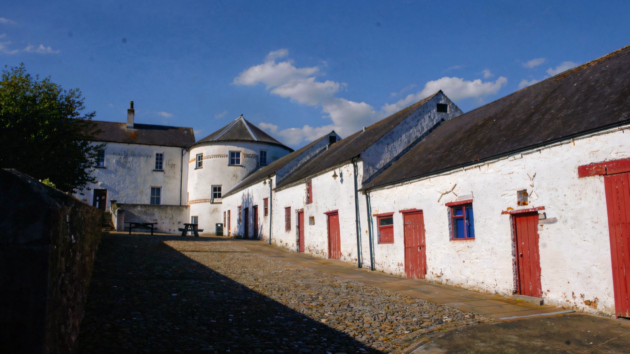 The cobbled courtyard lane at Bellaghy Bawn, red-doored outbuildings on the right and the round tower behind