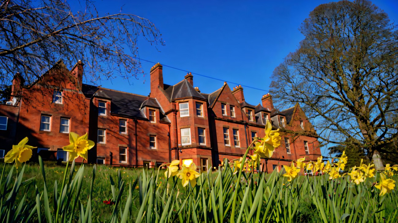 The red-brick Servite Priory building at Benburb behind a bank of daffodils under a blue sky