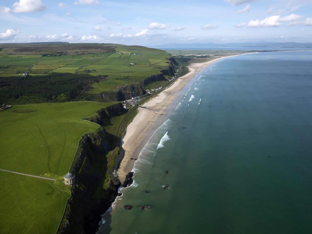 Aerial view of Benone Strand curving for miles below Mussenden Temple towards Magilligan Point and the Donegal hills