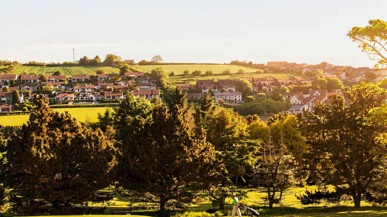 A golfer walks the fairway with Whitehead's rooftops on the hillside behind