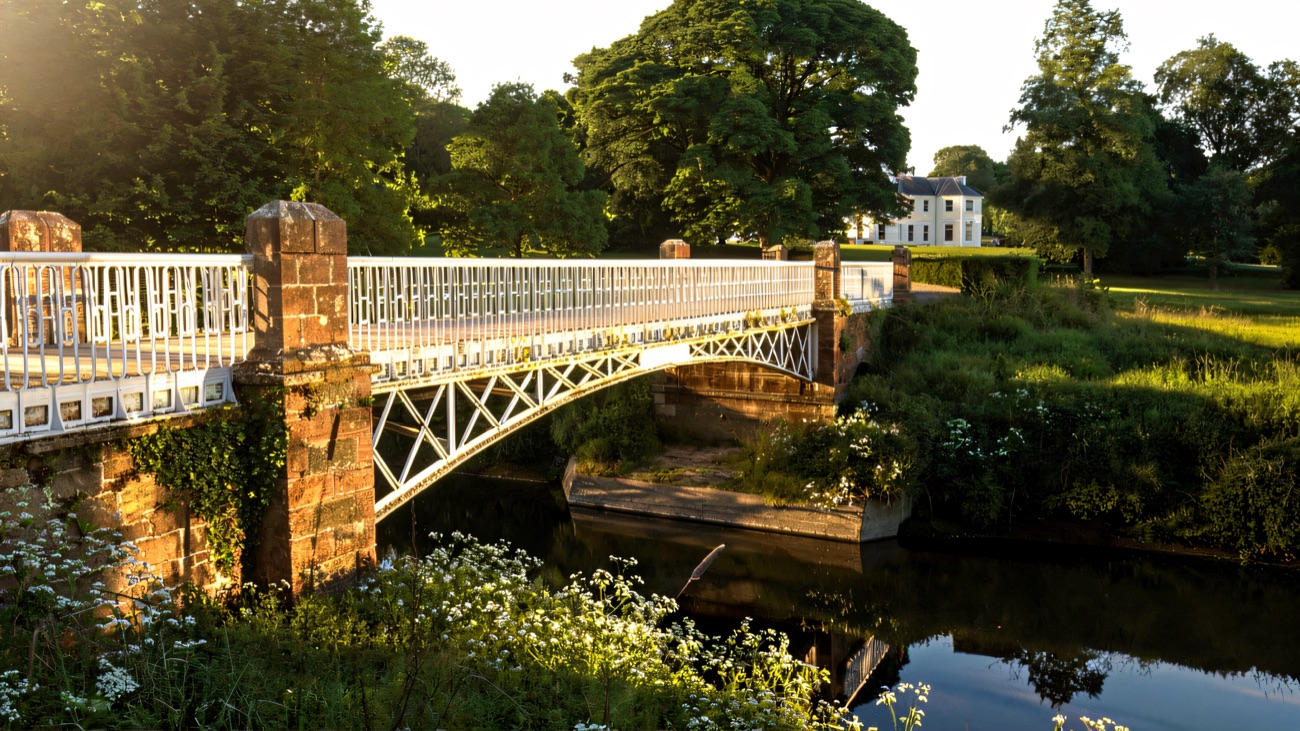 The white iron bridge over the River Bush with the house beyond