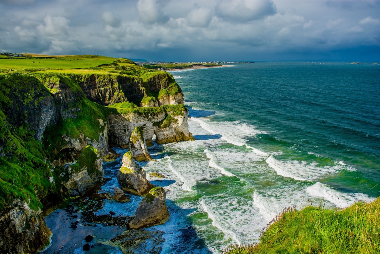 White limestone cliffs and sea stacks above rolling green waves at Whiterocks Beach with Portrush in the distance