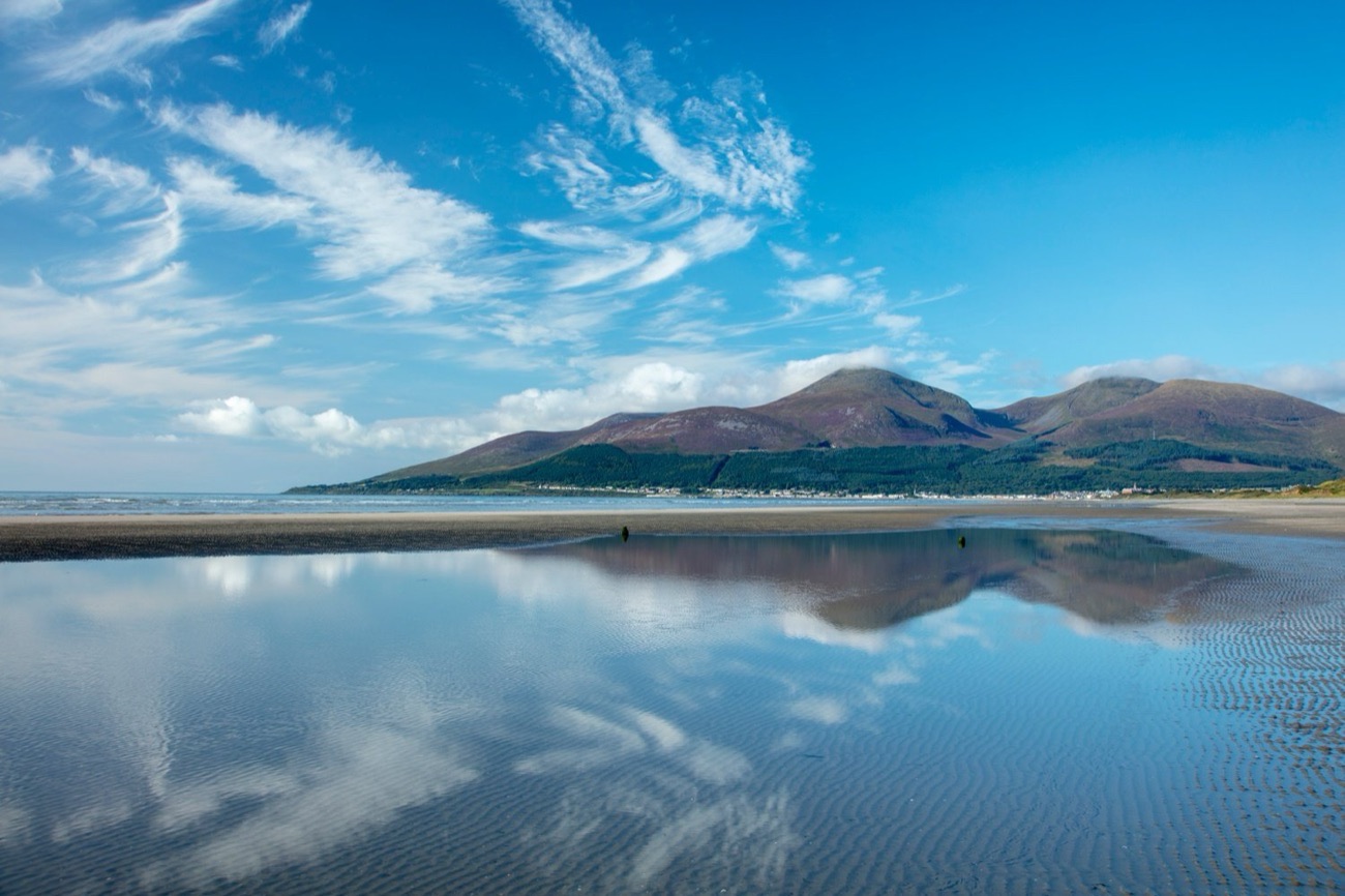 Blue sky and clouds reflected in tidal pools on Newcastle Beach with the Mourne Mountains and the town beyond