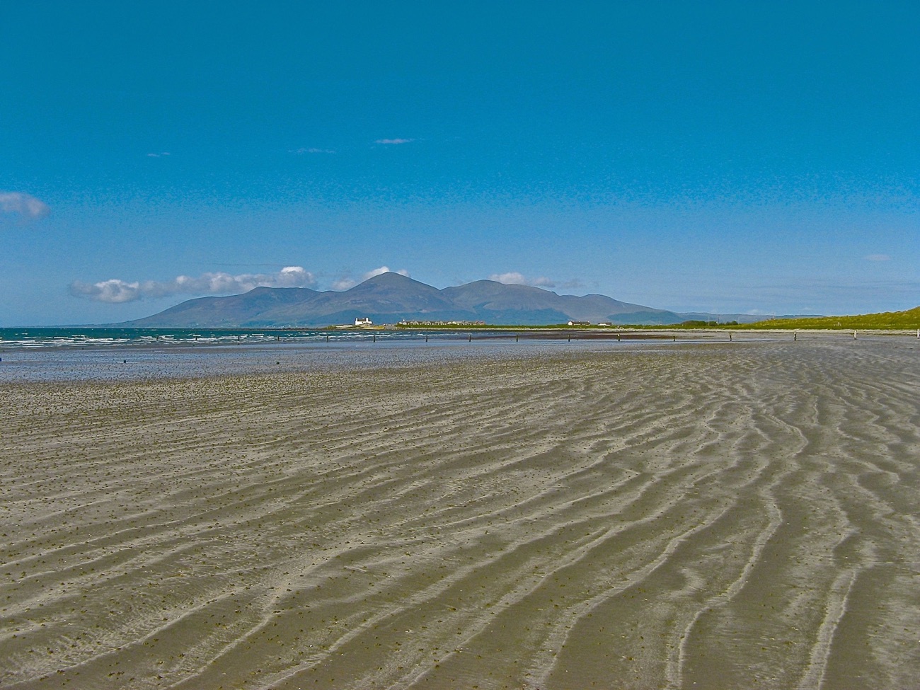 The flat open sand of Tyrella Beach under a blue sky with the Mourne Mountains across Dundrum Bay
