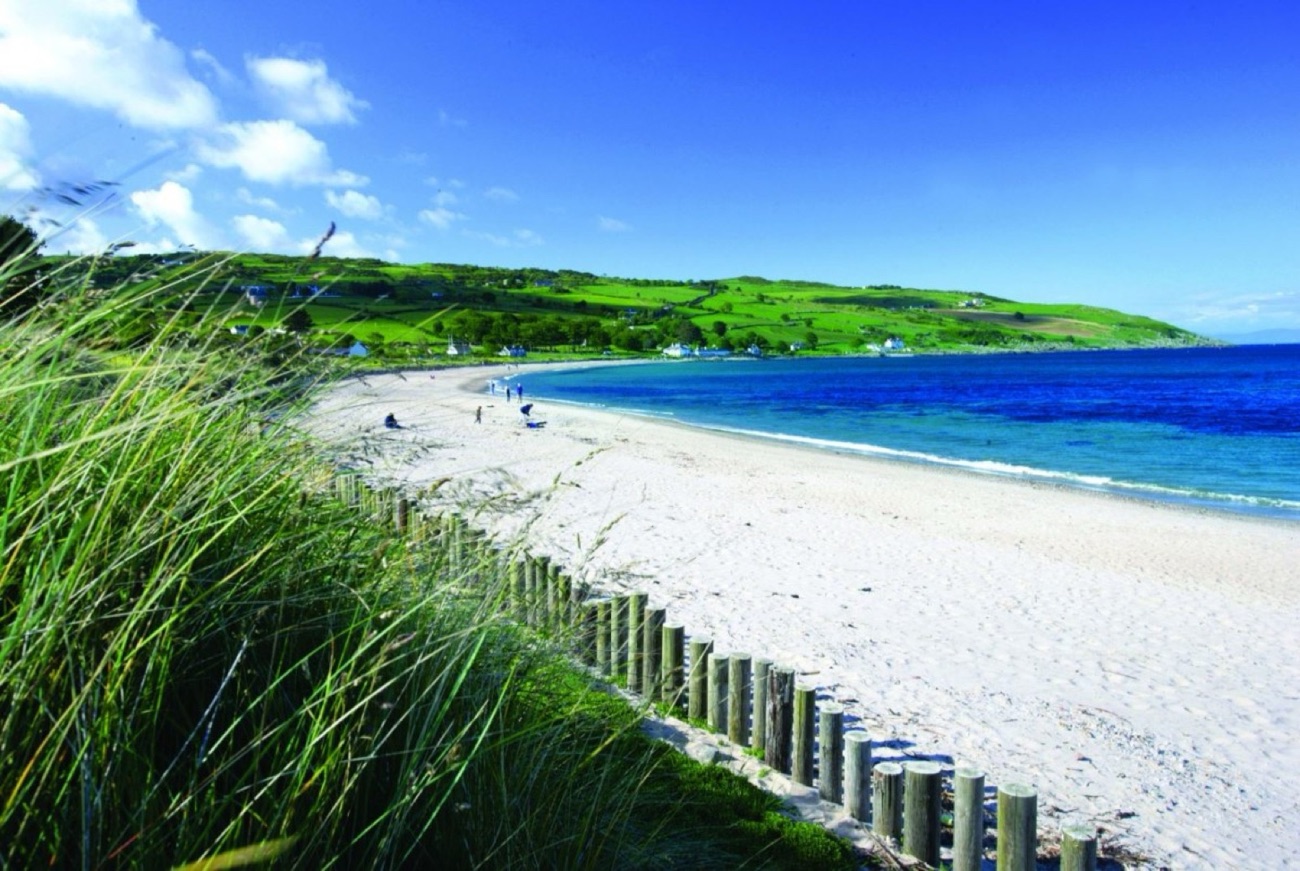 White sand and blue water at Cushendun Beach with the green hills of the Glens of Antrim behind