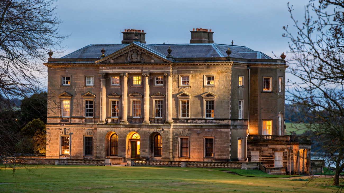 The Classical front of Castle Ward house lit warmly at dusk across the lawn