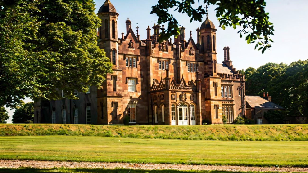 The turreted sandstone front of Glenarm Castle seen across the lawn between summer trees