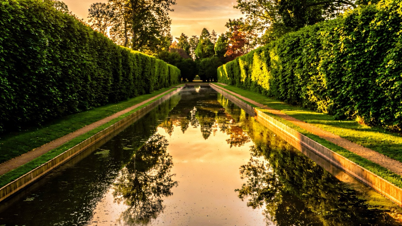 The long mirror-still ornamental canal at Antrim Castle Gardens between towering clipped hedges at sunset