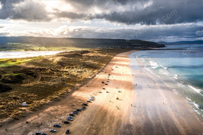 Aerial view of cars parked along the sand at Portstewart Strand under dramatic light