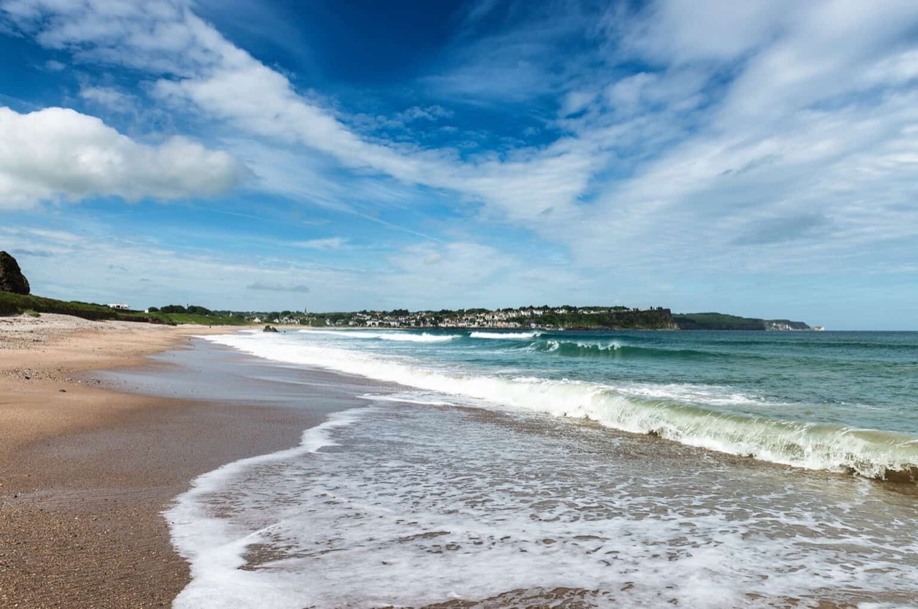 Ballycastle Beach looking along the sand towards the rocky far end, with the coast rising beyond