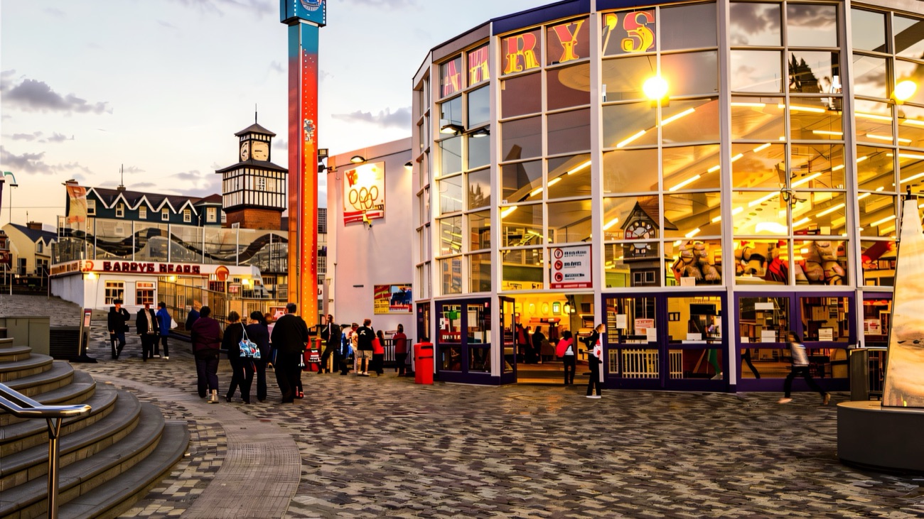 The glowing glass front of Curry's Fun Park in Portrush at dusk with families outside