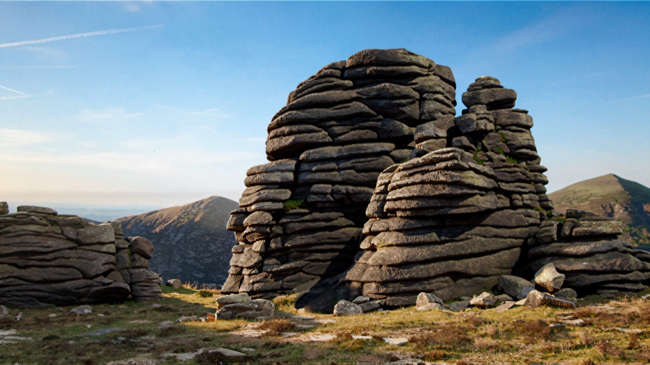 A tall stack of layered granite standing on the grassy summit ridge, with Mourne peaks behind.