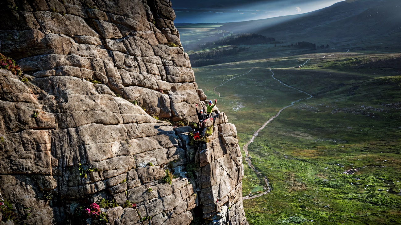 The steep granite crag face with tiny climbers on a ledge, looking down over the valley and forest.
