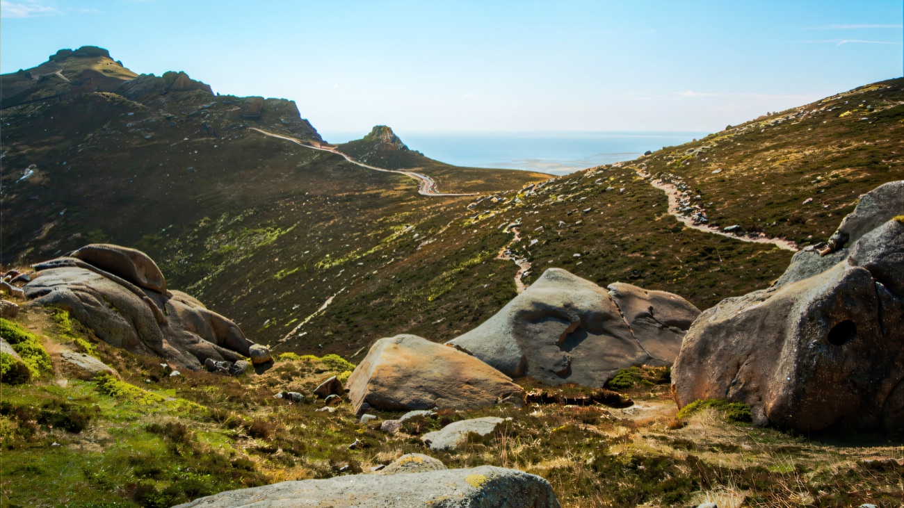Granite boulders scattered along the ridge, with the path dropping away toward the sea in the distance.