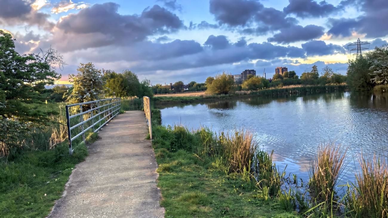 A railed path running along the water's edge, the city rising in the distance