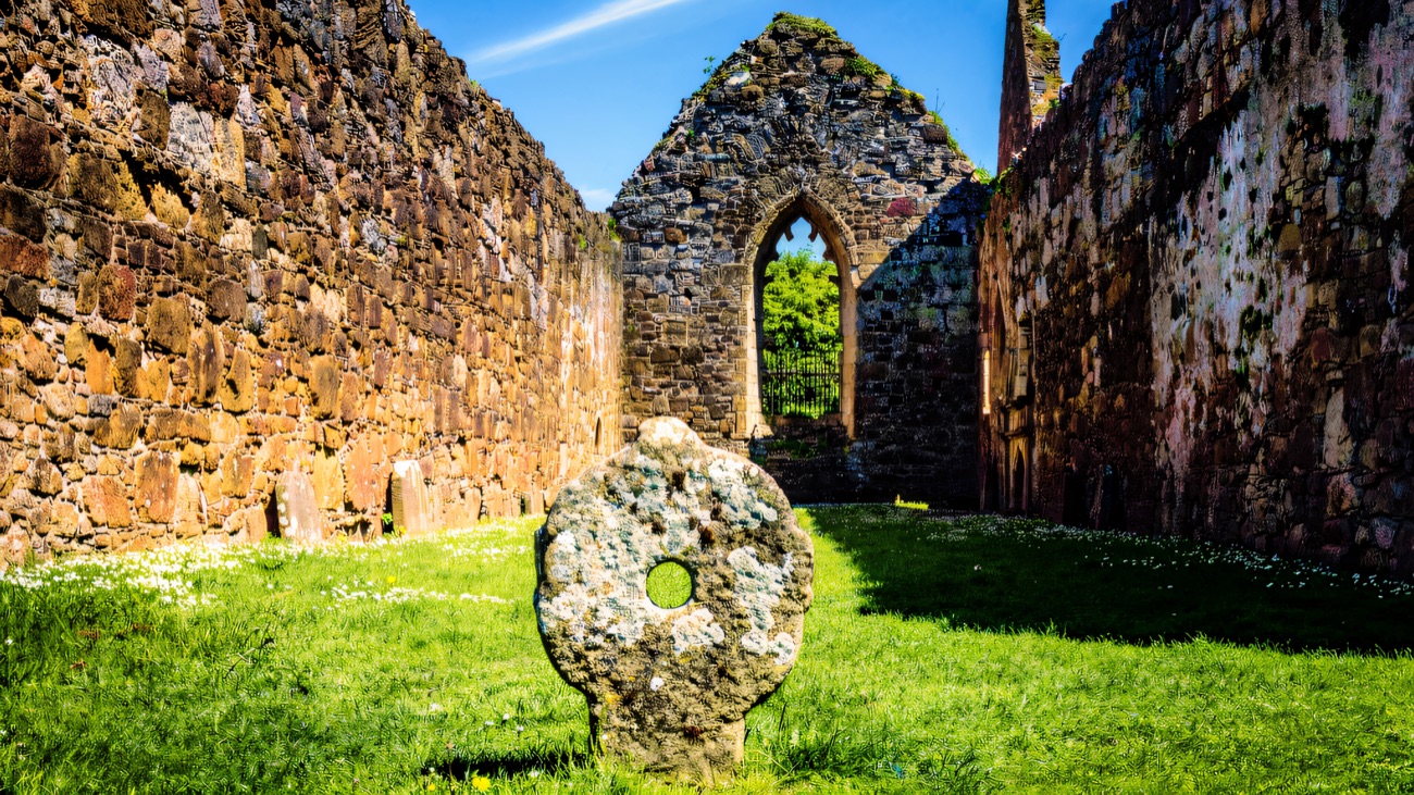 Inside the friary, a pierced ring-cross stone on the grass before a Gothic window