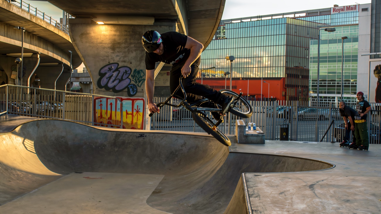 A helmeted BMX rider airing out of the bowl under the flyover