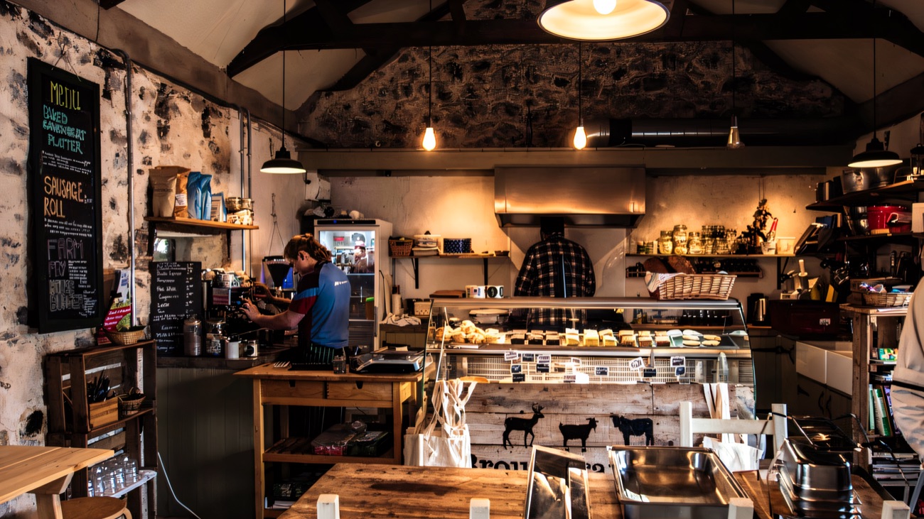 The café counter and deli in the stone barn, with fresh bread, bakes and a coffee machine under pendant lights