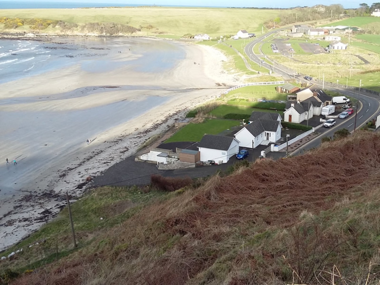 An elevated view over the whole horseshoe of Browns Bay with the coast road and car park behind the sand